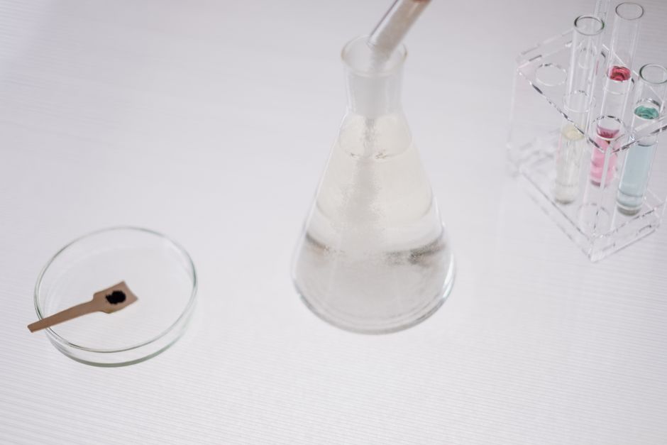Close-up of laboratory glassware including a flask, test tubes, and petri dish on a white surface.